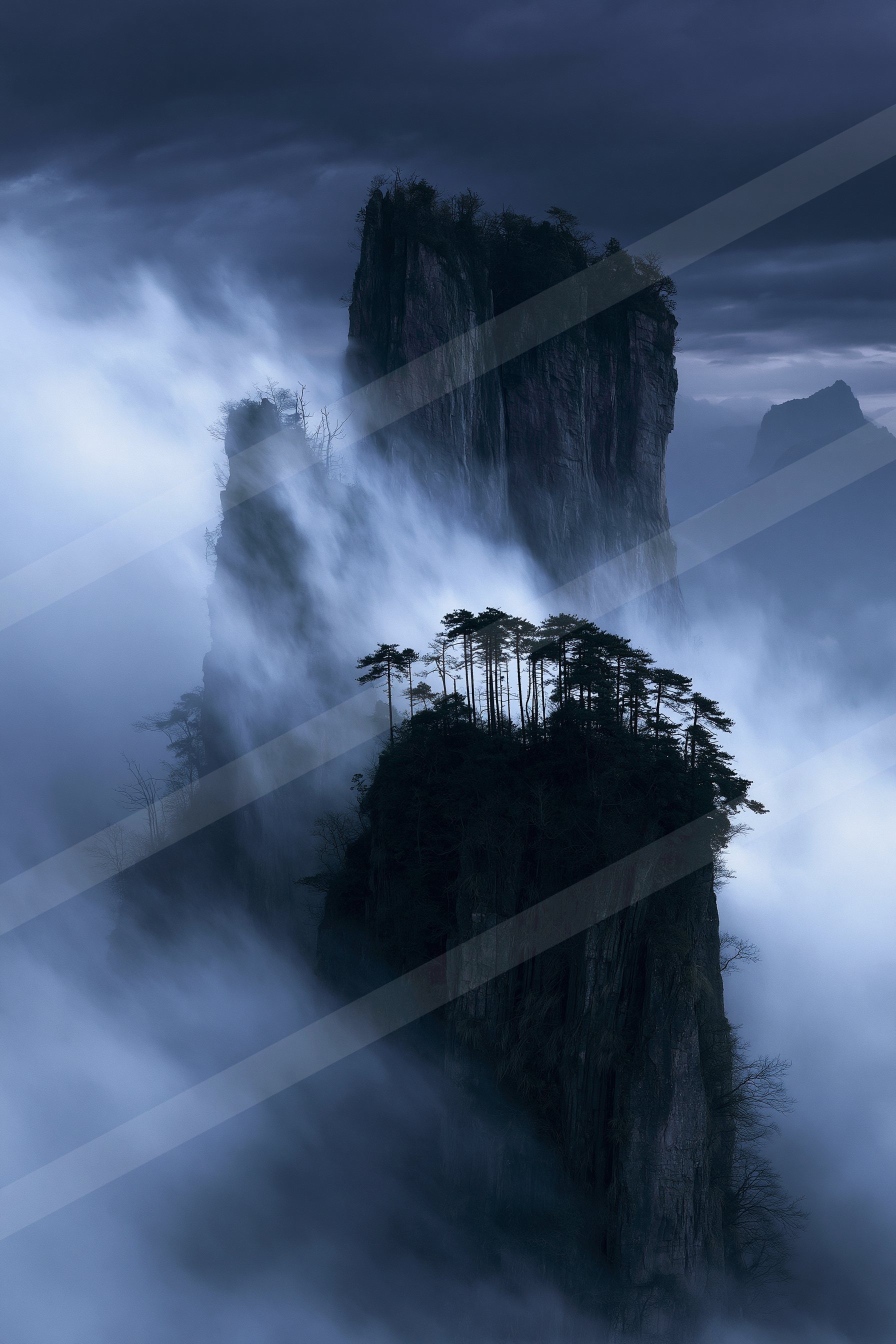 A towering mountain peak shrouded in mist during dusk, featuring a forested cliff edge and rugged rock formations.