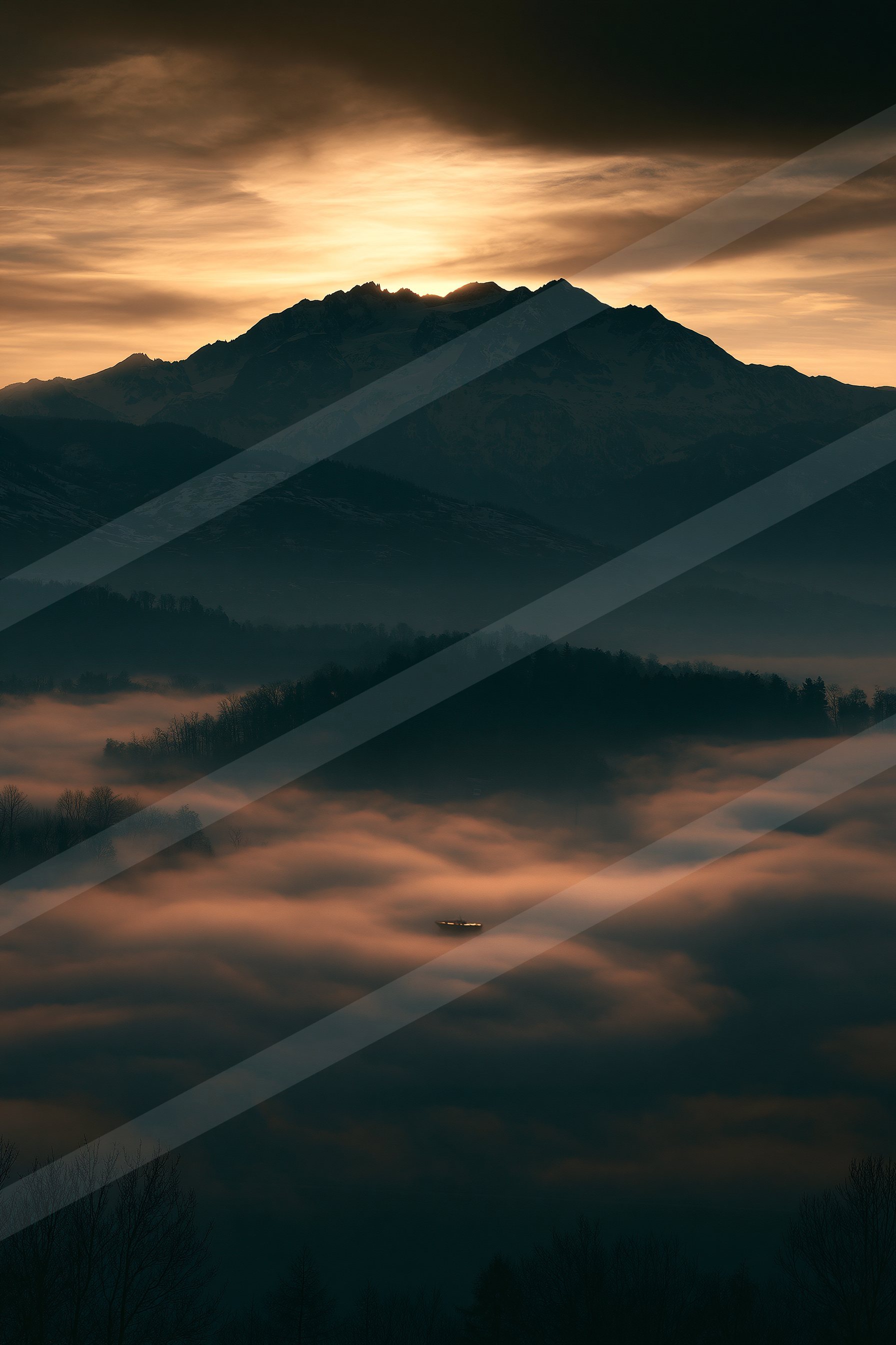 A majestic mountain range silhouetted against a vibrant sunset sky, with misty clouds filling the valley below.