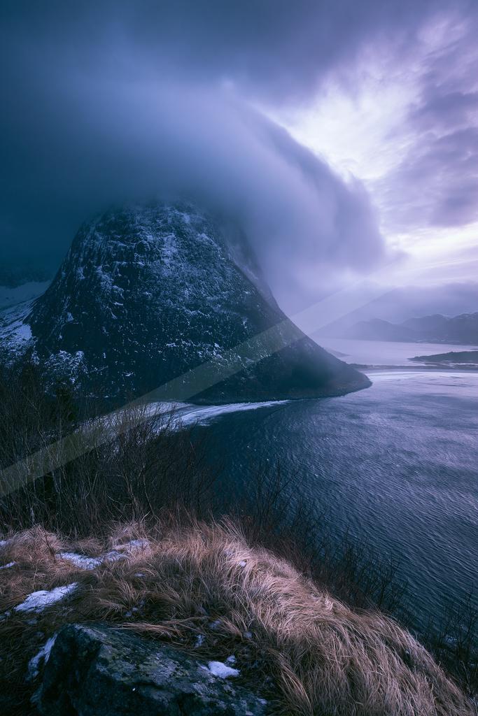 A blue hour landscape of mountains, storm, ocean.