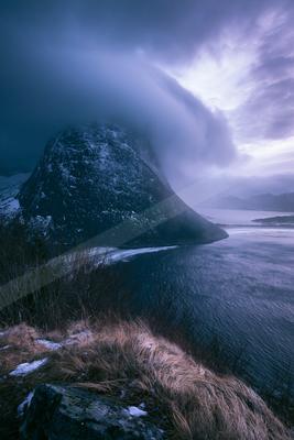 A blue hour landscape of mountains, storm, ocean.