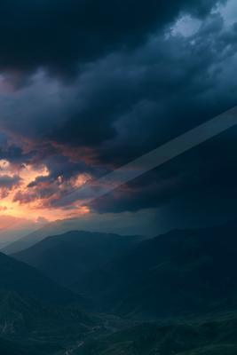 A blue hour sky scene of sunset, mountains, storm.
