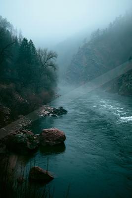 A green-toned moody photograph of valley, cliff, dam.