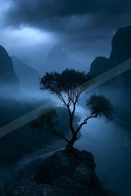A blue hour nature scene of trees, mountains, river.