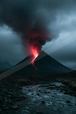 A powerful volcanic eruption at dusk, with bright red lava flowing down the mountainside and a massive plume of dark smoke rising into the cloudy sky, above a r
