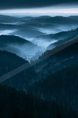 A blue hour landscape of mountains, valley, fog.