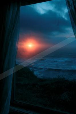 View from a window with curtains of a dramatic red sun setting over a stormy ocean with large waves and dark blue clouds.