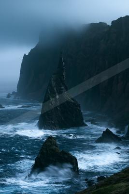A mysterious high contrast water scene of a coastline, fog.