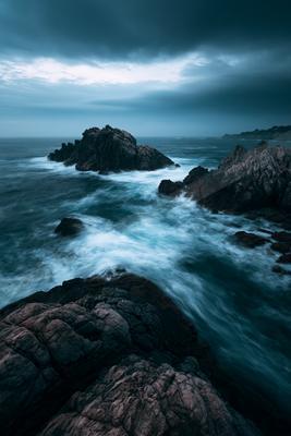 A blue hour long exposure water scene of ocean, rocks.