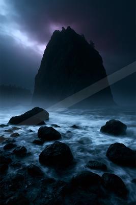 A tall rocky sea stack rises from a turbulent ocean under a dark, stormy sky with purple and blue hues, surrounded by mist and foreground rocks in churning whit