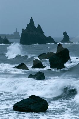 A blue hour water scene of ocean, beach, rocks.