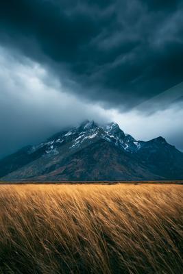 A dramatic long exposure landscape of mountains, field, storm.