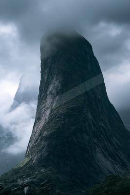A towering mountain peak shrouded in misty clouds against a dark, moody sky.