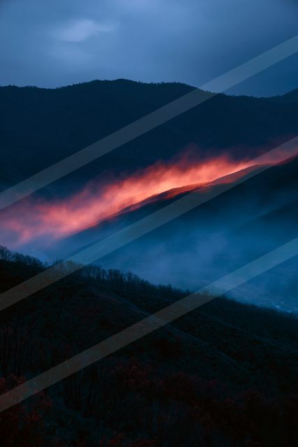 A mountain range shrouded in atmospheric red mist against a dark blue twilight sky, creating a striking contrast.