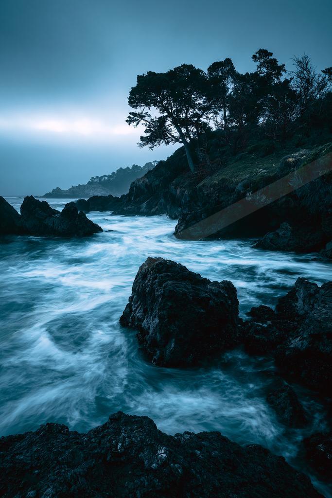 A blue hour long exposure water scene of a coastline, rocks.