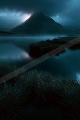 A dramatic, dark mountain peak rises above a thick layer of fog over a calm lake, with dramatic light breaking through heavy storm clouds in a moody blue landsc