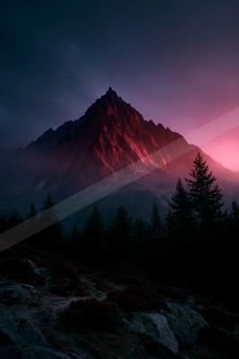 A sharp rocky mountain peak illuminated in intense red light against a dark purple and pink twilight sky, with silhouetted evergreen trees in the foreground.