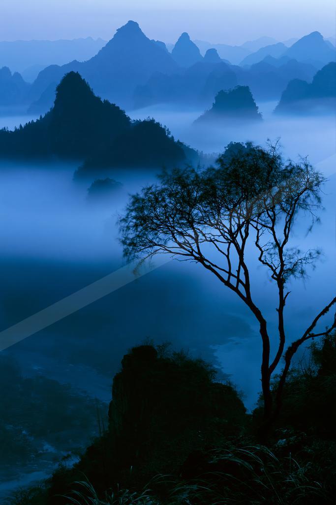 A blue hour landscape of mountains, valley, trees.