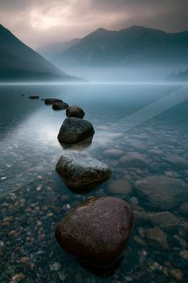 A serene water scene of lake, mountains, waterfall.
