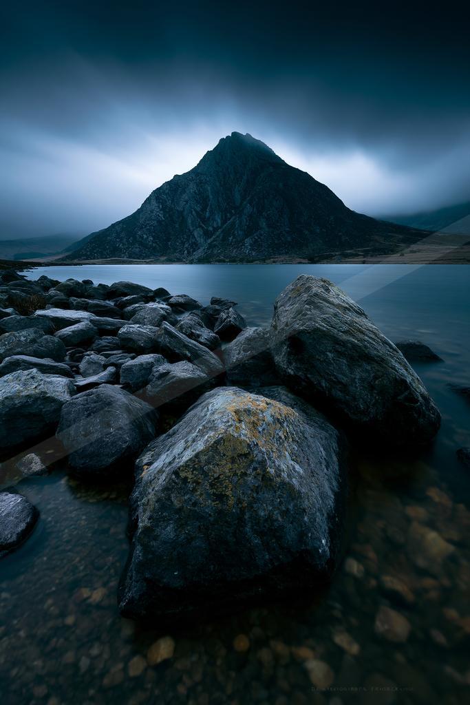 A blue hour long exposure water scene of lake, mountains, rocks.