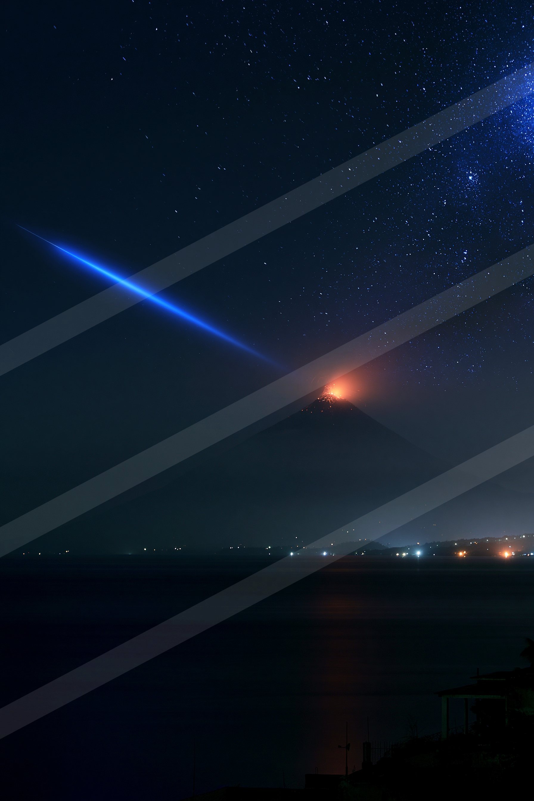 A volcano erupting with glowing lava under a star-filled night sky, featuring a prominent blue star trail and reflections on the water below.