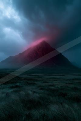 A rugged mountain peak glows with intense red light against a dark, stormy sky, with a moody foreground of windswept grass and heather.