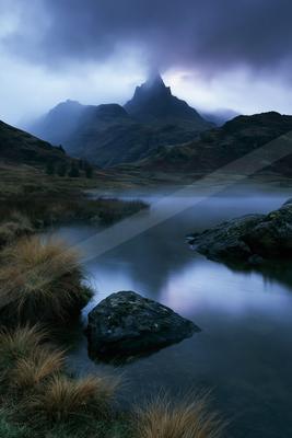 A blue hour long exposure landscape of mountains, lake, fog.