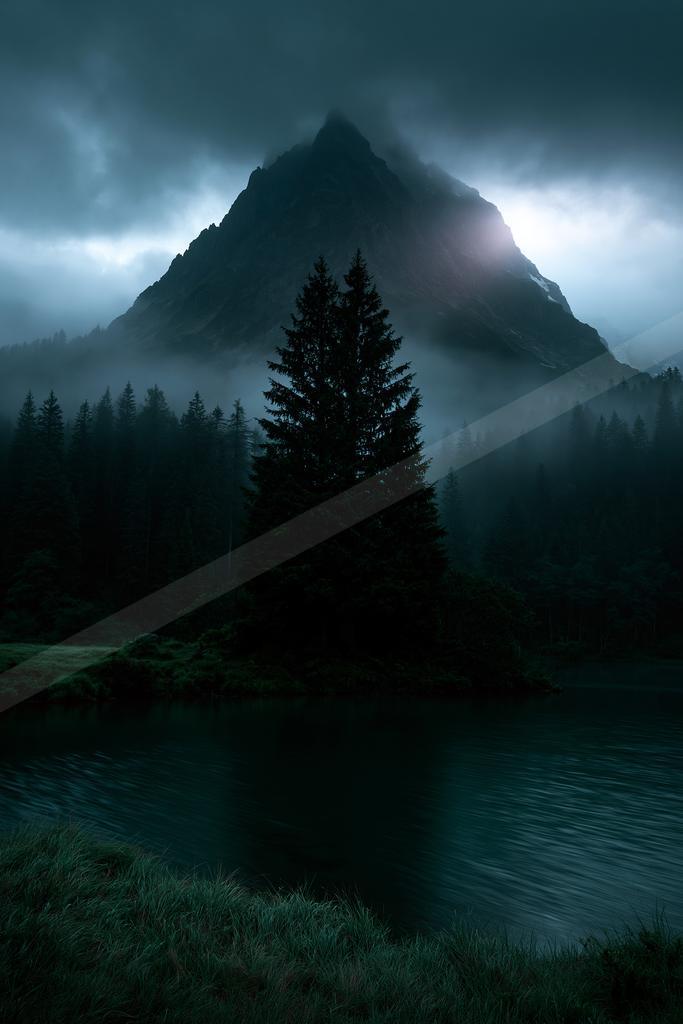 A tall dark coniferous tree stands in the foreground beside a calm lake, with a massive misty mountain peak rising behind a dense forest under brooding clouds.