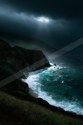 Moody coastal landscape featuring rugged cliffs, a small sandy beach, and turquoise ocean waves crashing under a dark stormy sky with dramatic light rays breaki