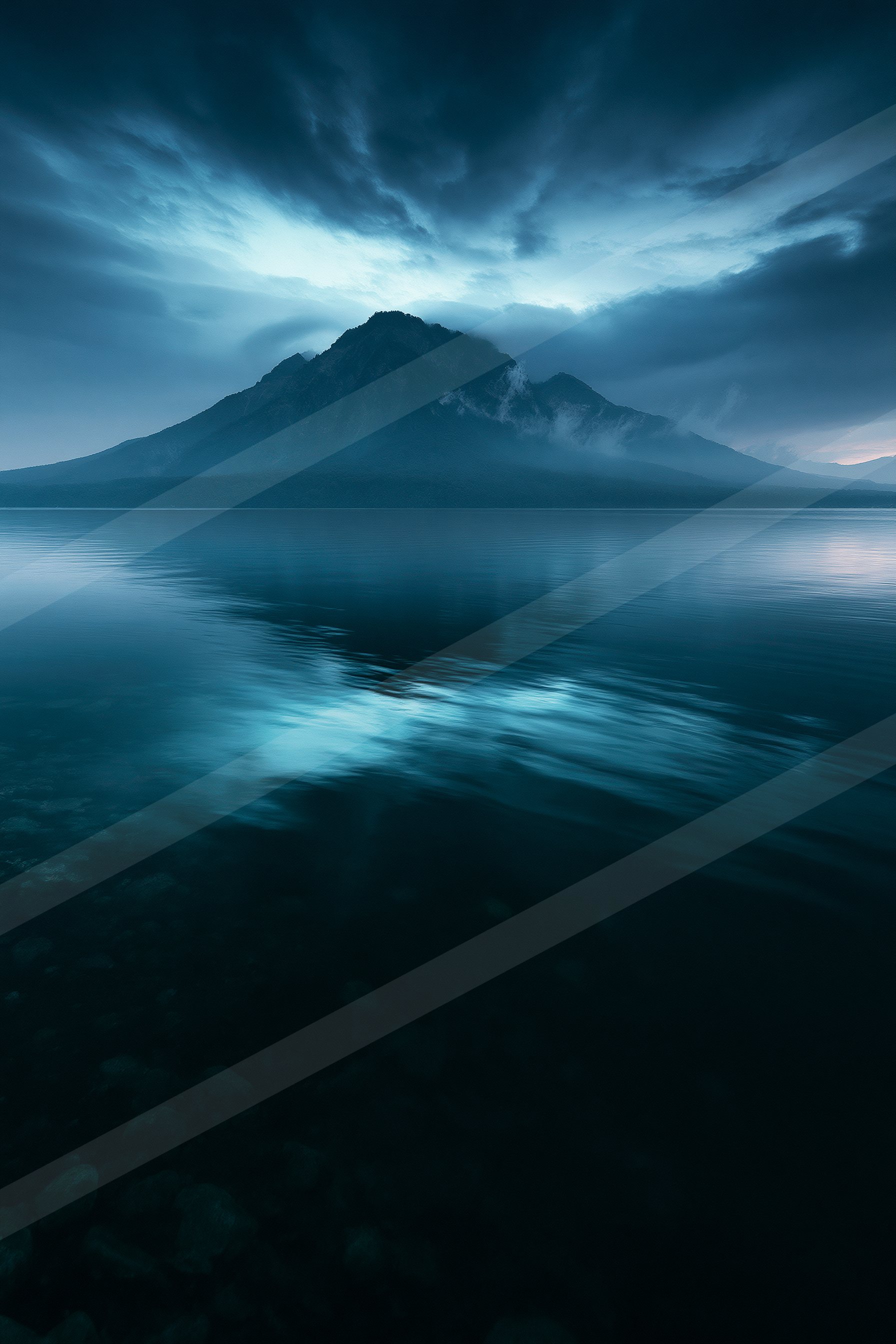A serene lake reflects a majestic mountain under a moody twilight sky.