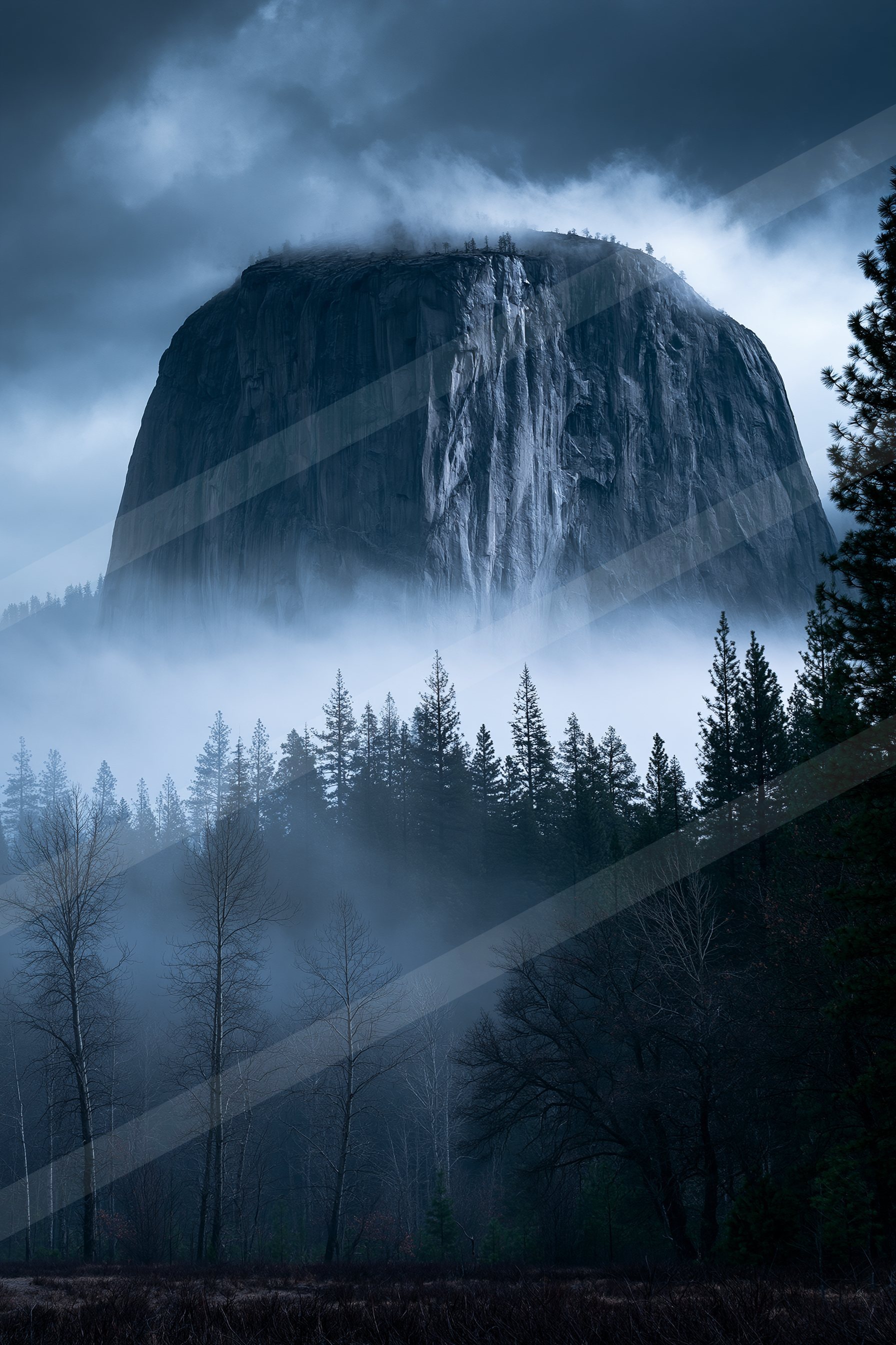 A towering mountain peak rises above a dense forest shrouded in mist, under a dark, cloudy sky.