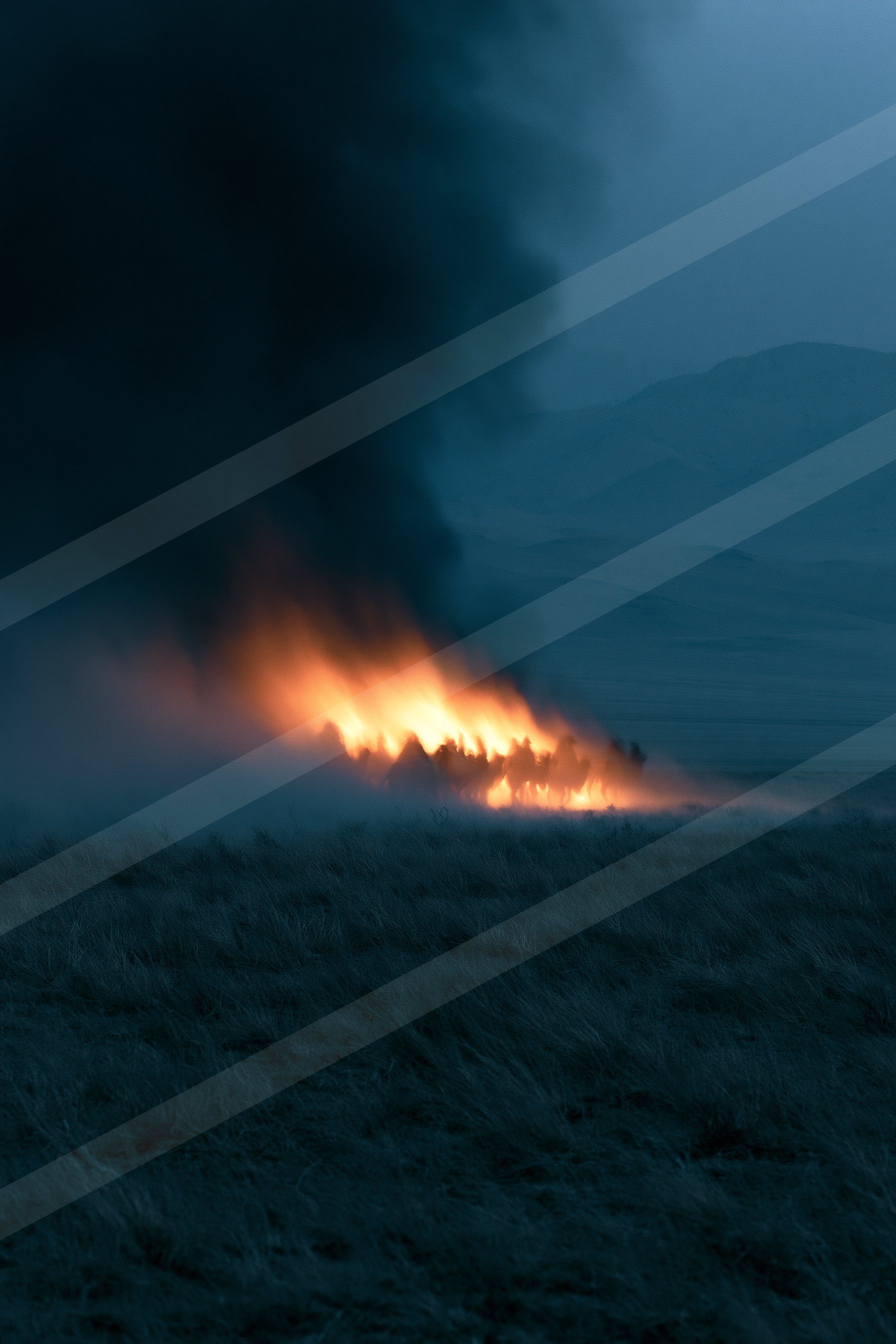 A large fire burns brightly against the dark backdrop of a mountainous landscape.