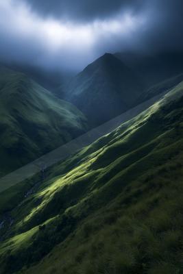 A moody landscape of mountains, valley, field.