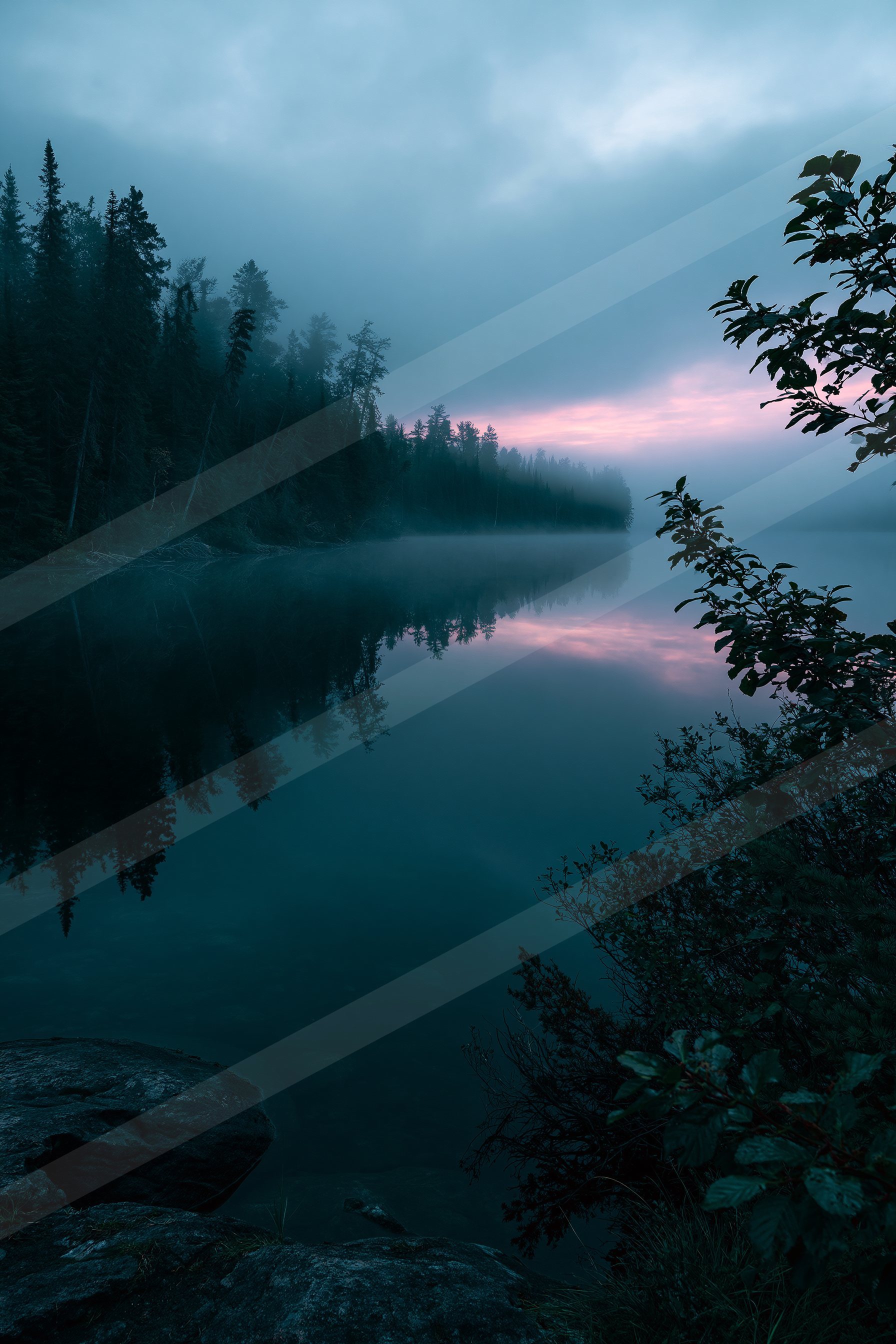 A serene lake shrouded in mist reflects a forested shoreline and a soft pink sunrise, creating a tranquil atmosphere.