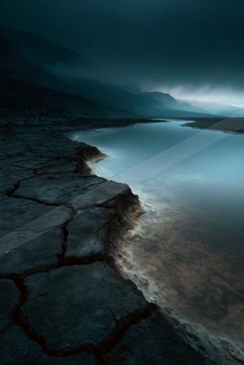 A black-toned moody photograph of breakwater, lakeside, beacon.