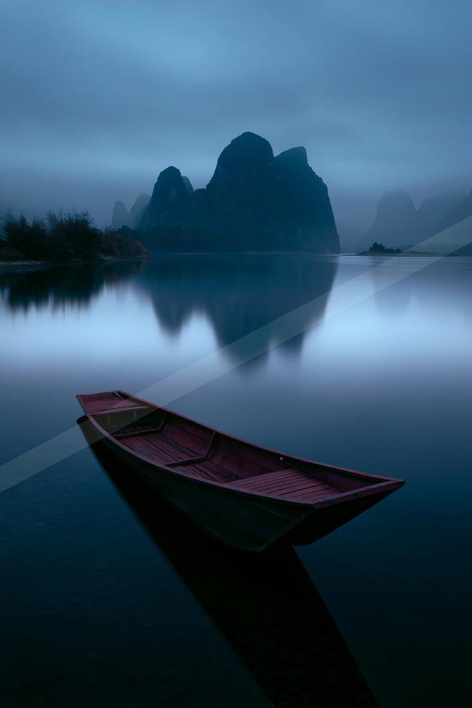 A black-toned moody photograph of canoe, paddle, lakeside.