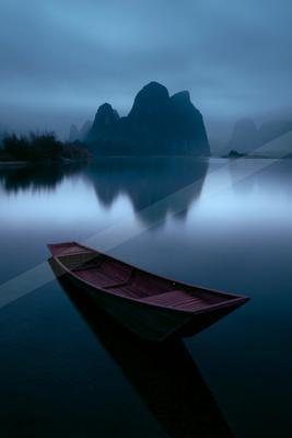 A black-toned moody photograph of canoe, paddle, lakeside.