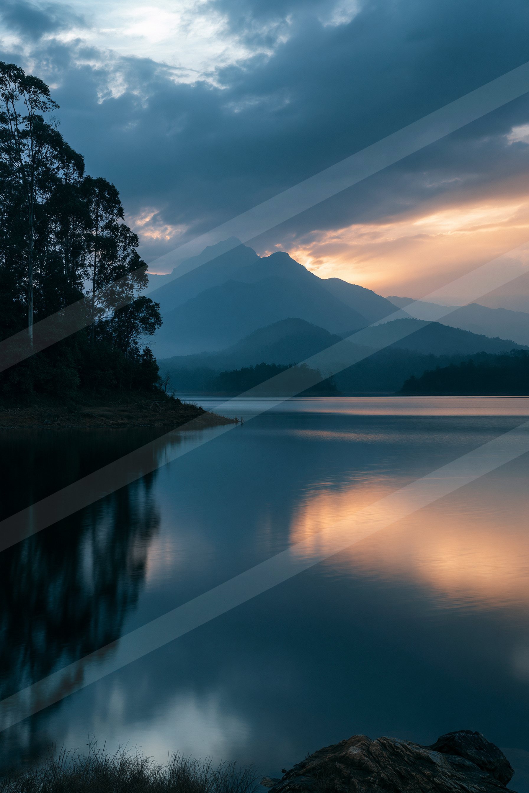 A tranquil lake reflects the vibrant hues of a sunset sky with silhouetted trees and distant mountains.