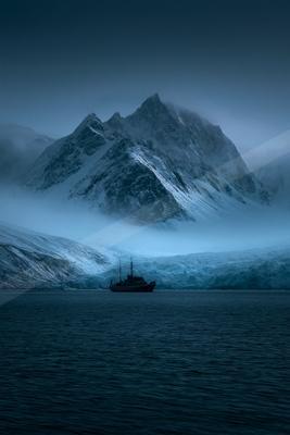 A blue hour landscape of mountains, ocean, fog.