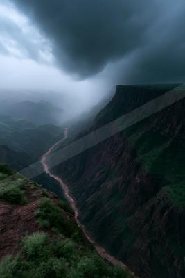 Moody atmospheric view of a deep river canyon with steep rocky cliffs and green vegetation under heavy dark storm clouds and mist.