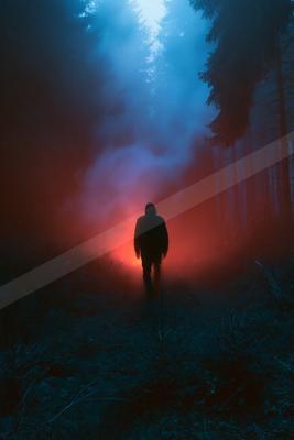 A lone figure walks through a forest enveloped in fog, illuminated by vibrant red and blue lights.