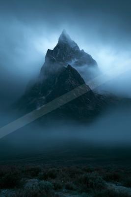 A dramatic landscape of mountains, fog.