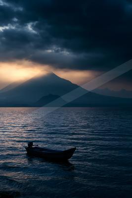 A black-toned moody photograph of canoe, volcano, paddle.