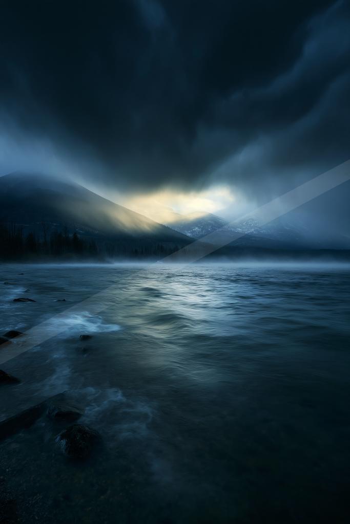 A blue hour sky scene of storm, mountains, lake.