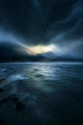 A blue hour sky scene of storm, mountains, lake.