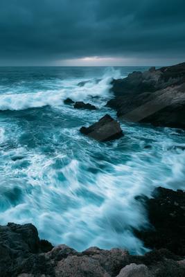 Powerful waves crashing against rugged cliffs under a moody twilight sky.