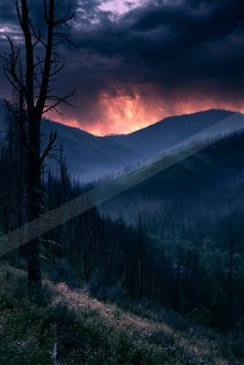 A moody landscape of mountains, valley, sunset.