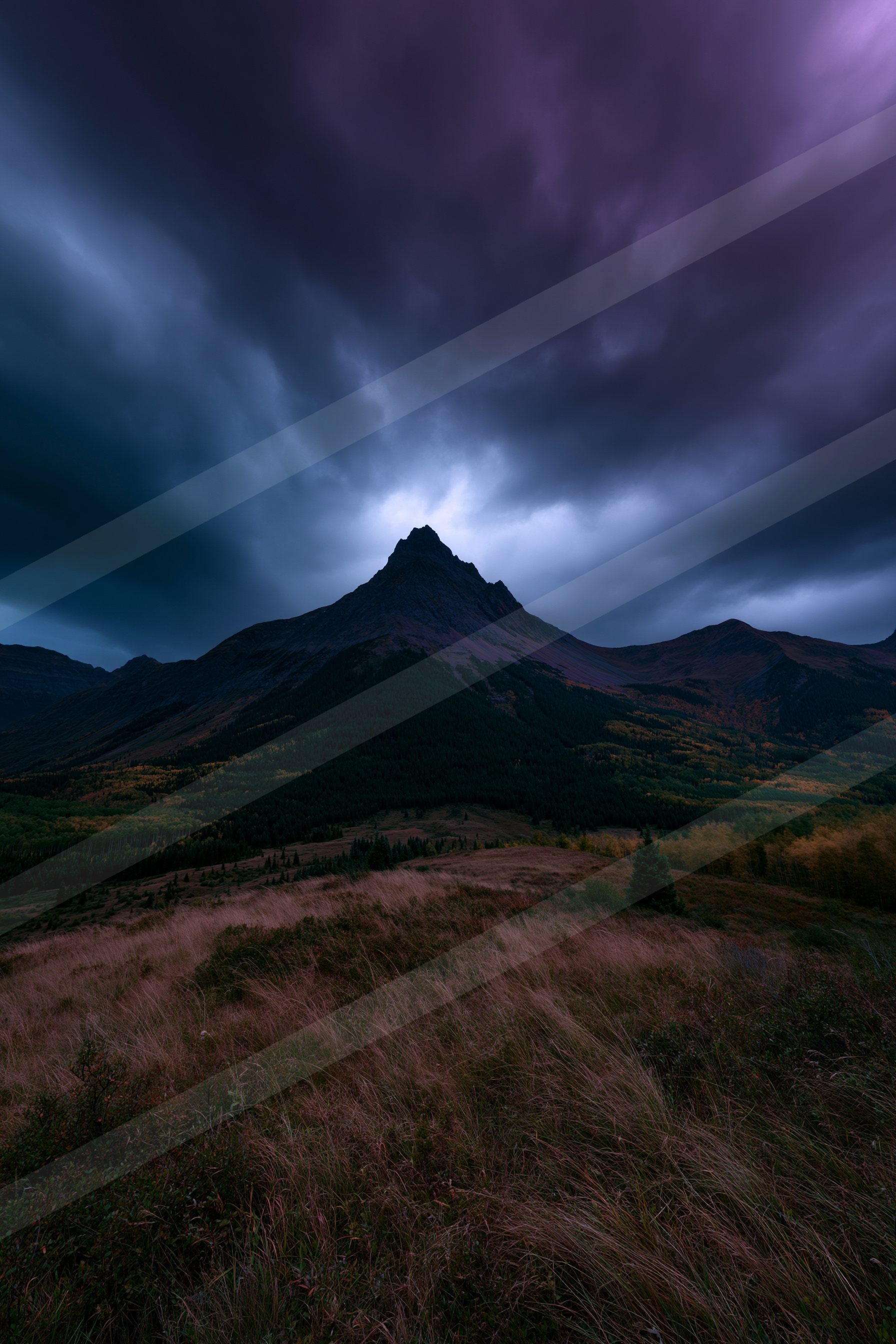 A rugged mountain peak stands tall under a dark, moody sky filled with swirling clouds.