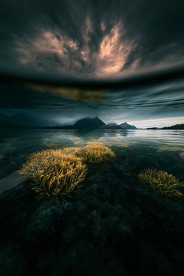 A moody water scene of ocean, mountains, clouds.
