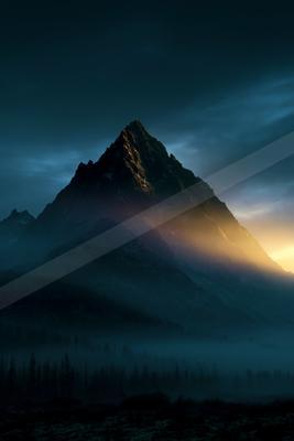 A sharp rocky mountain peak illuminated by golden sunrise light piercing through heavy blue fog and mist, with a dark forest visible in the valley below.