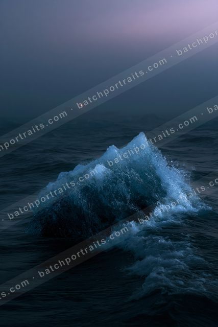 A striking iceberg illuminated by a red light glows against the dark, calm ocean during twilight.